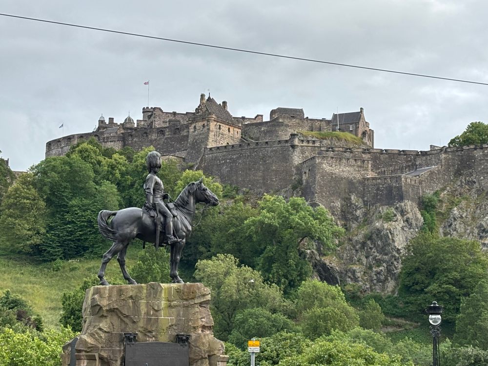 A castle on a hill. In front is a statue of a man on a horse