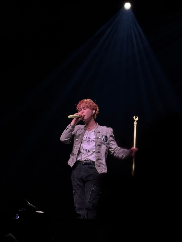shinee’s onew at percent london. he is singing into his mic while holding the mic stand beside him.