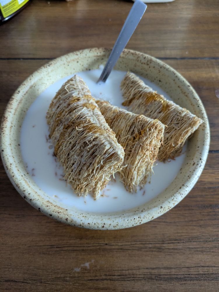 A bowl of cereal, with three shredded wheat biscuits filling the bowl. 