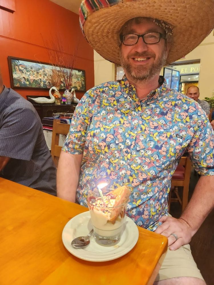 Me in my goofy (no pun intended) Disney shirt and a sombrero, grinning with a cup of ice cream, a churro, and a lit candle.