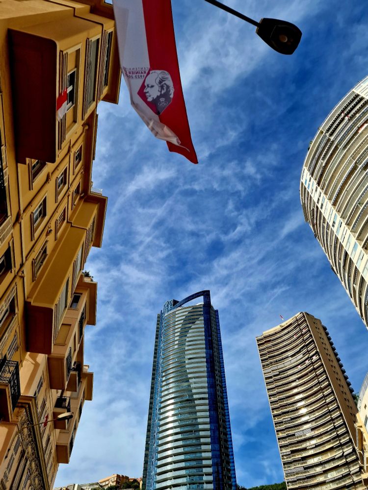 Vue en contre plongée de tours à Monaco, avec la Tour Odeon au centre, et un drapeau en hommage au Prince Rainier en haut de de la photo