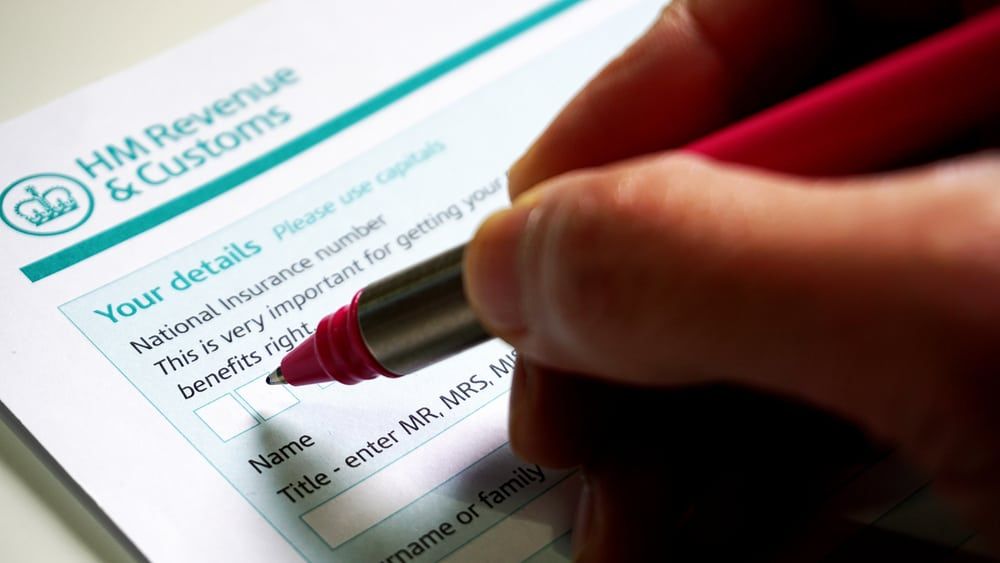 Image shows a hand with a red pen attempting to fill in a HM revenue and customs form.