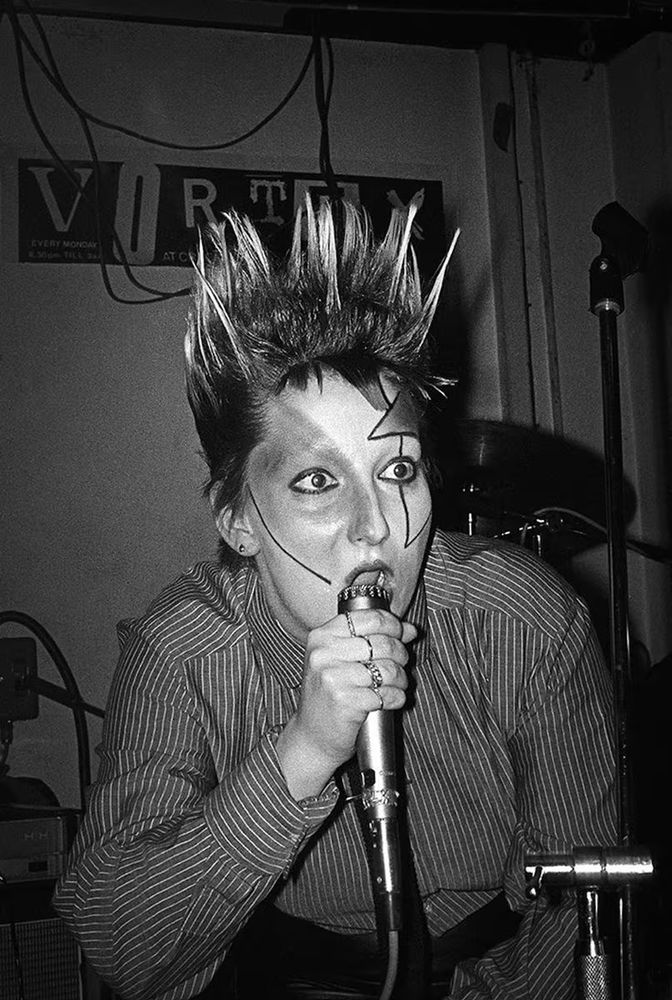 Punk icon Pamela Rooke, AKA Jordan, holding a microphone with her signature spiked up hair and geometric makeup.