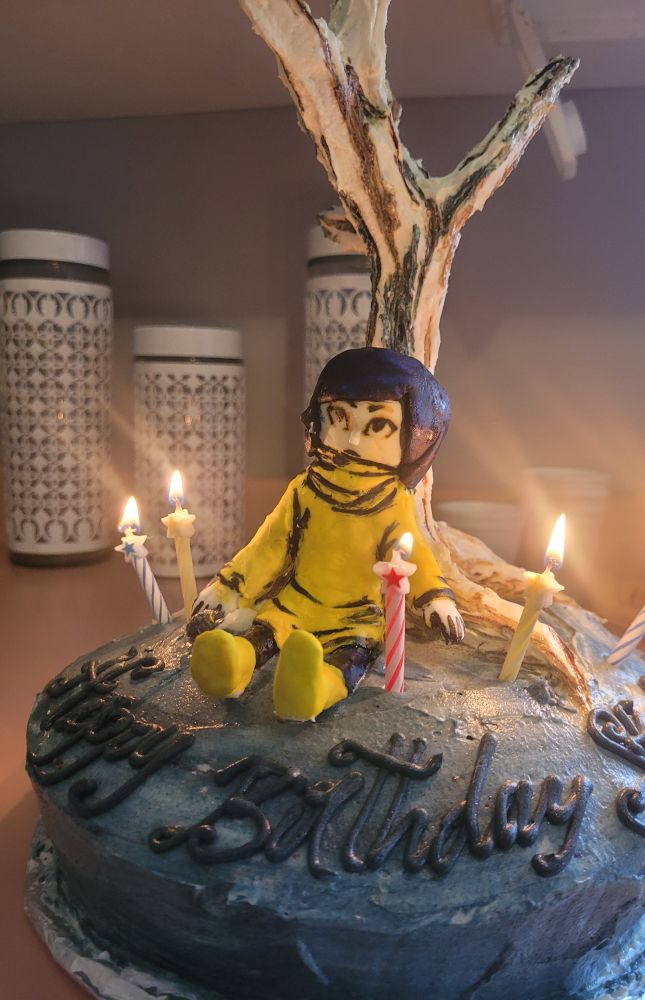 Coraline birthday cake! 
Coraline is actually a cake pop sitting on a single layer cake and the tree is actually tin foil in the shape of a tree and covered in icing cause the rice crispies were NOT COOPERATING. 
A few candles surround her. 