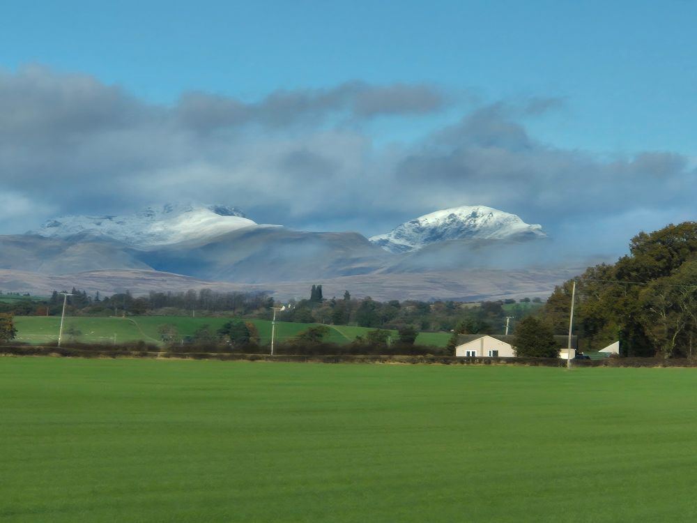 Imagine of a green field, with a small, white cottage to the viewer's right. In the distance are two snowcapped hills. Taken from just outside of Stirling, Scotland. 