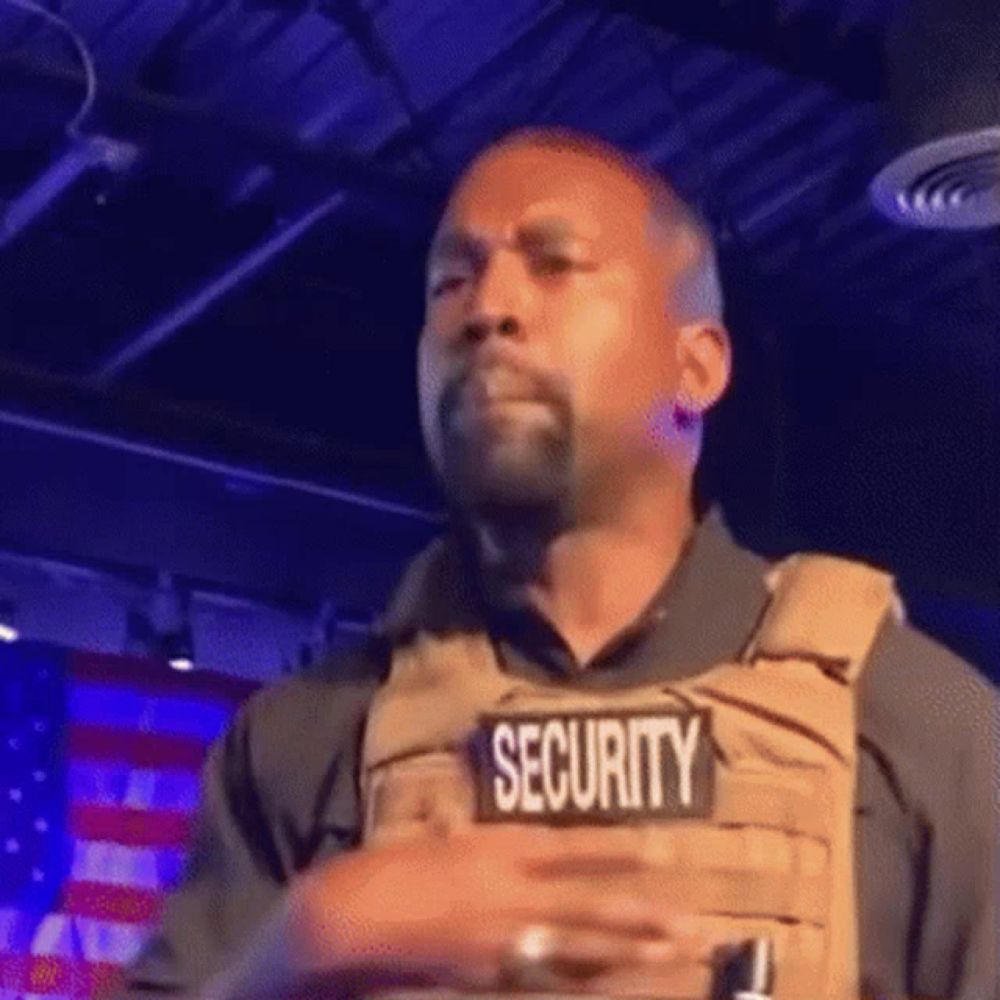 kanye west is wearing a security vest while standing on a stage .