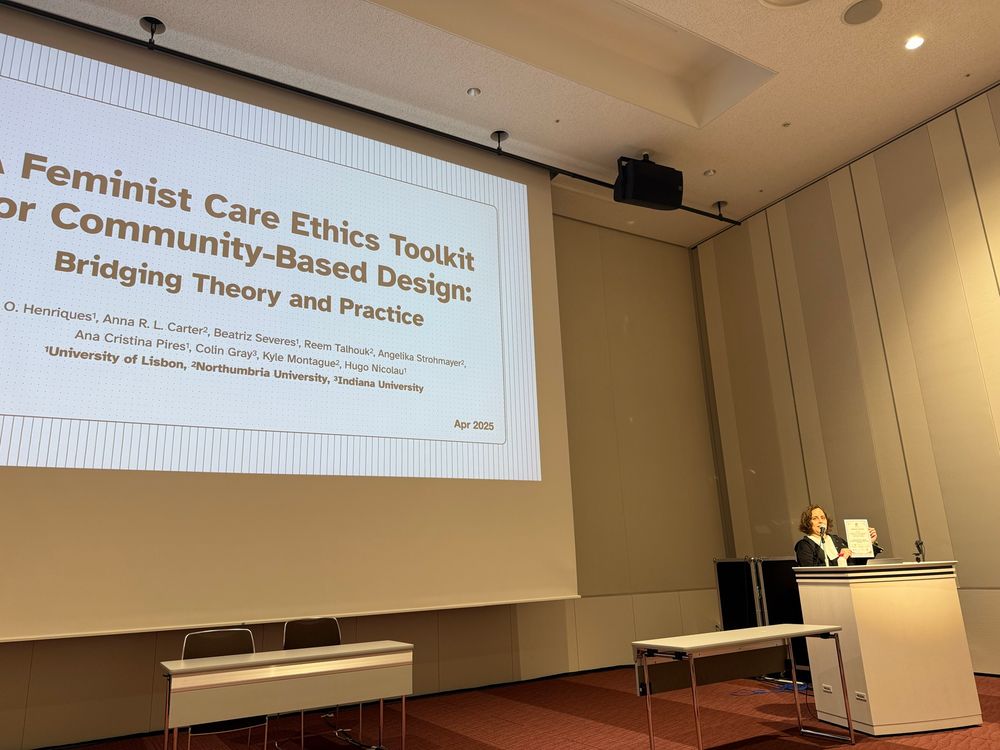 Ana presenting the title slide of the presentation on a feminist care ethics toolkit and holding up an honorable mention award. 