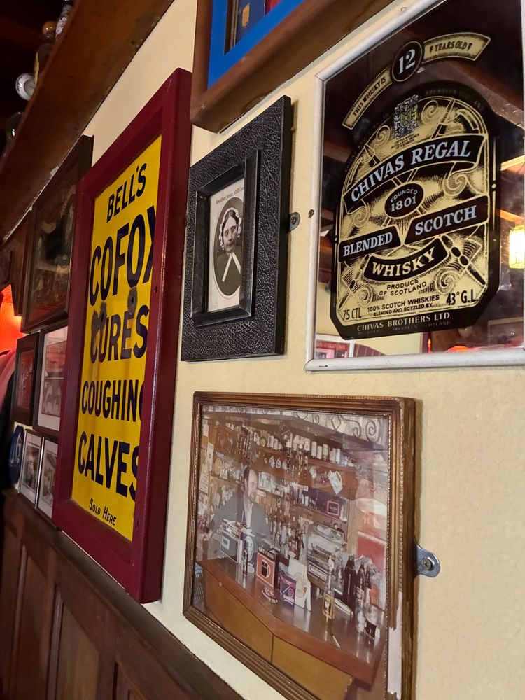 Back wall of the front of the pub. Photographs, and an advertisement declaring BELLS COFOX CURES COUGHING CALVES