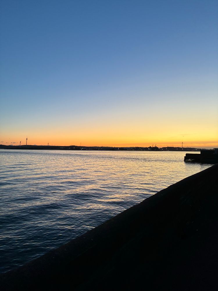Sunset over a harbour, flaming in the distance while turbines poke the sky