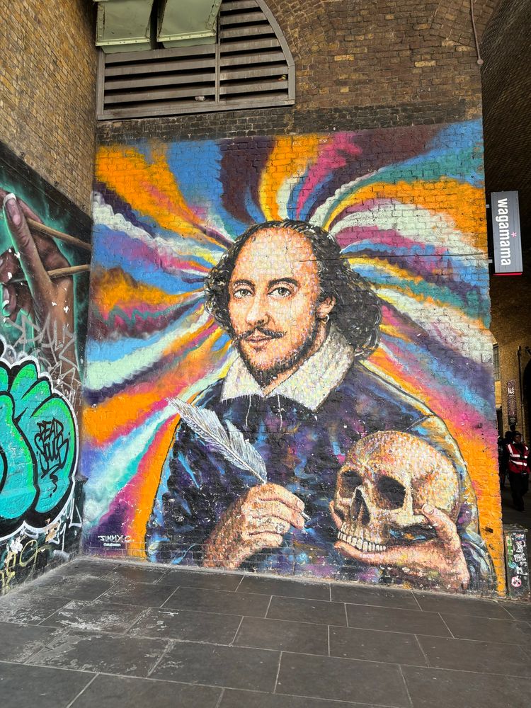 Photo (by David McInnis) of Australian artist Jimmy C’s famous mural of Shakespeare in Clink Street near the Globe. It depicts Shakespeare as known via the Chandos portrait, holding a skull like Hamlet does, and a quill, in front of a psychedelic swirl of colour.