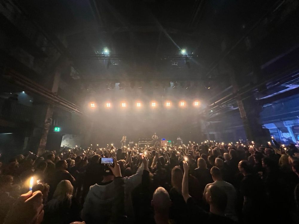 Konzert in einer Halle, abgedunkelt, die Fans  halten Feuerzeuge in die Höhe. 
Strahler über der Bühne leuchten zur Menschenmenge