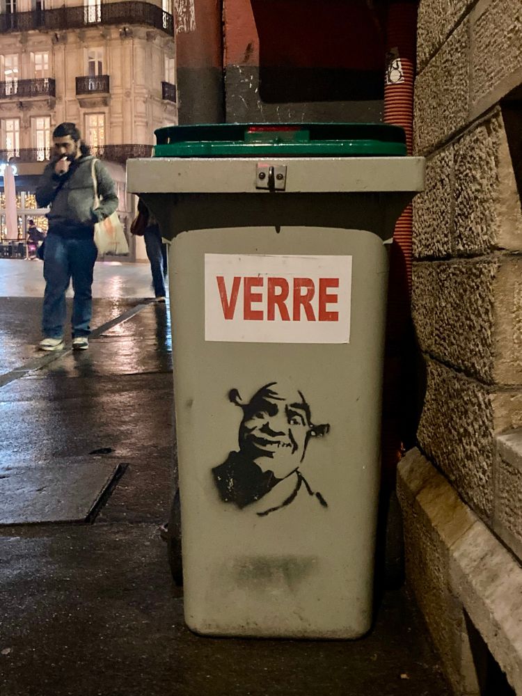 Conteneur à verre avec un graffiti stencil de Shrek et au dessus l’indication « verre ». 