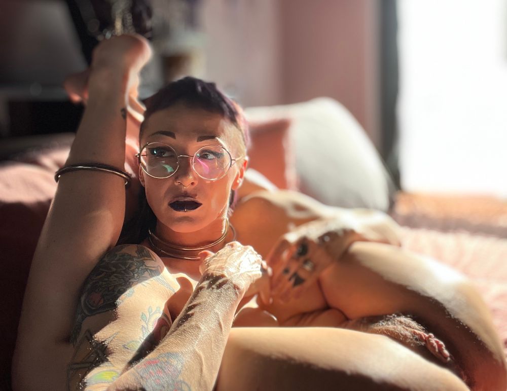 Nat reclines in bed- her legs thrown back and resting, ankles locked, behind her head- her arms rest comfortably on the backs of her thighs and she looks casually off frame left, her nude body glows in the bright sunlight- the veins in her arm and hand prominent, the tiny hairs on her pubic mound and surrounding her luscious lips sparkle, the tiny creases in her skin, the stretchmarks- all converging to great effect. A soft and textured photo of a fiend folded up but in repose. 