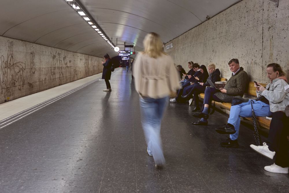 An older man sat waiting for a train glances up from his laptop as a woman passes by. Lumix S5iiX + Olympus 35 f.2.8