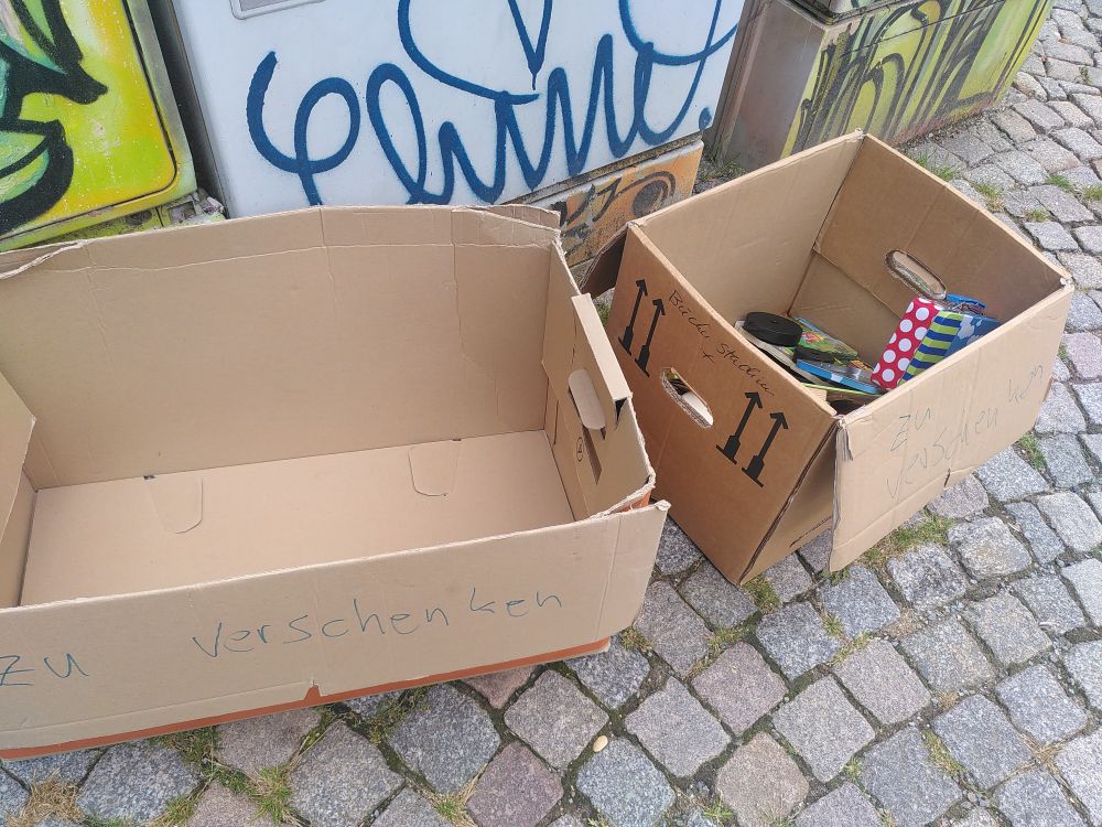 2 Kartons auf dem Gehweg, einer leer, im anderen noch wenige Spielsachen 