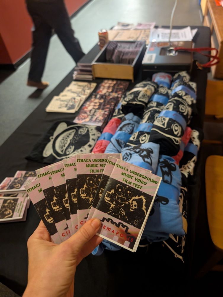 Table with merchandise and a small paper program for The Ithaca Music Video Film Festival.