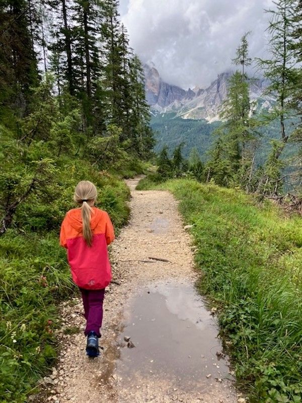 Mädchen im Regen im verregneten Cortina auf einem Waldweg im Sommer. Berge im Hintergrund, große Regenpfütze im Vordergrund des Bildes
