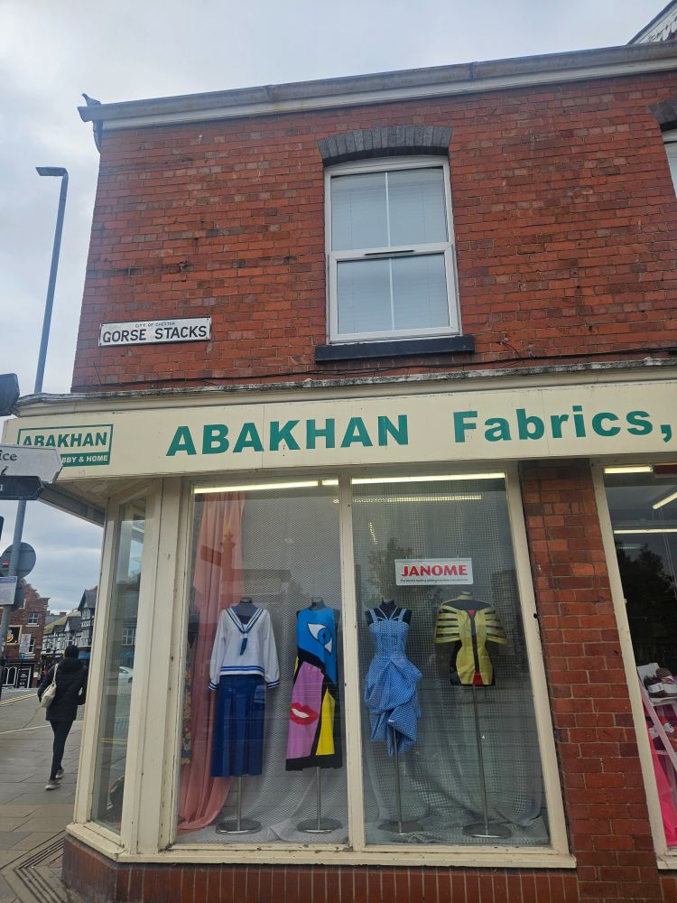Abakhan Fabrics shop display of dresses, red brick building on the corner of a busy street 