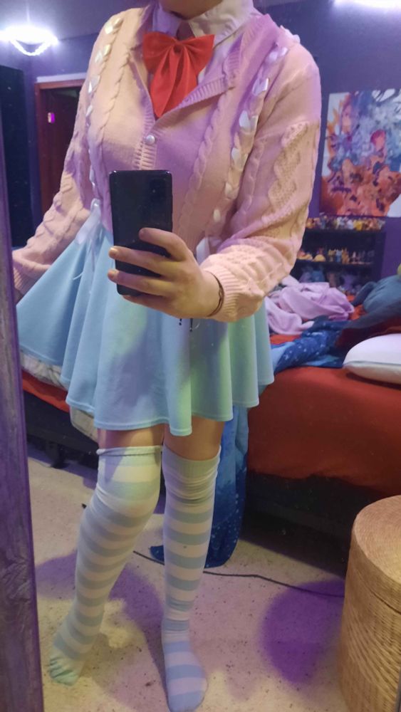 Irl Boco wearing Light blue and white striped socks, a light blue mini skirt, a white blouse with a red ribbion with a pink sweater with ribbons on top