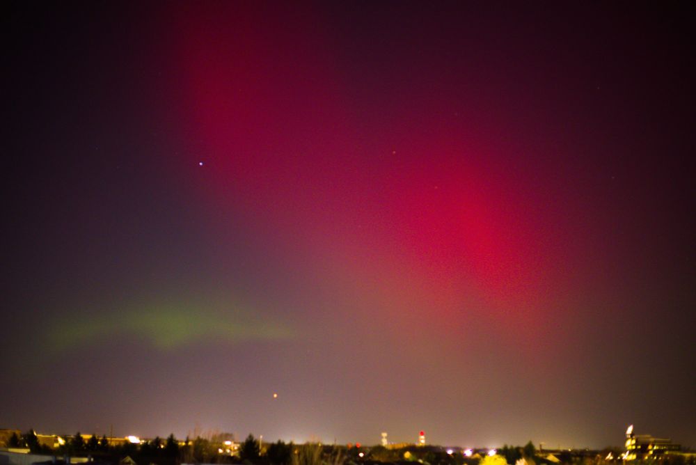 Northern lights over city, swooping red with small green band.