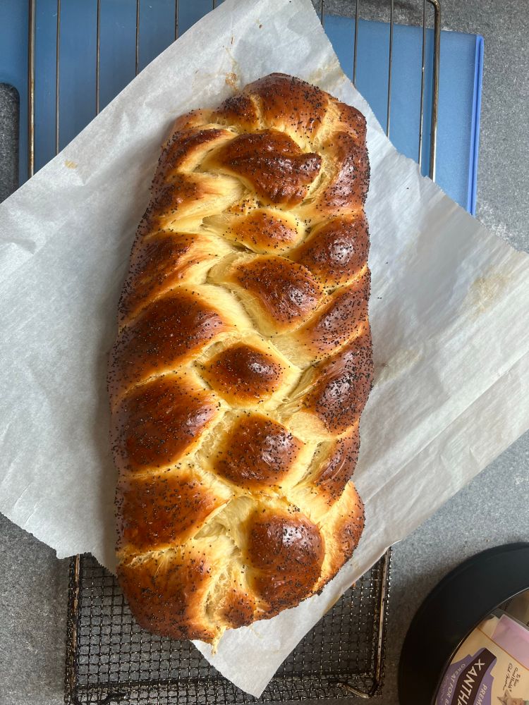 A photo of a six-strand poppyseed challah cooling on a piece of parchment paper.