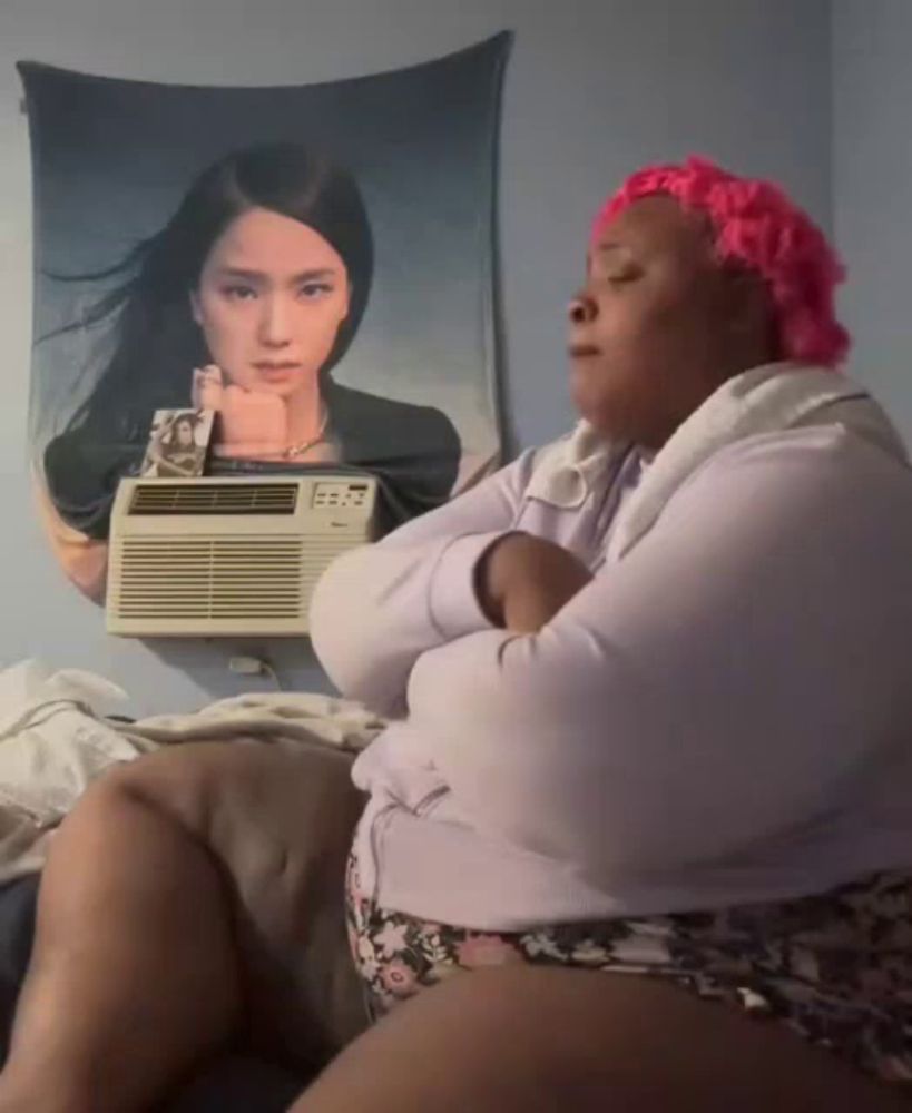 a woman with pink hair is sitting in front of an air conditioner and a painting of a woman