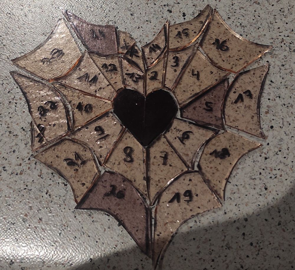 vitrail de pièces de verres numérotés formant une toile d'araignée en forme de coeur avec un cœur plus foncé au centre 