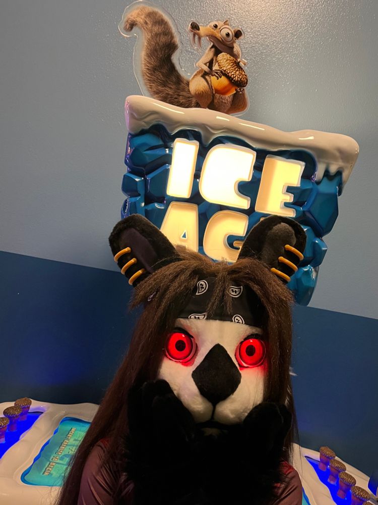 Angus the rabbit lurking in front of an Ice Age arcade game, featuring Scrat holding an acorn 