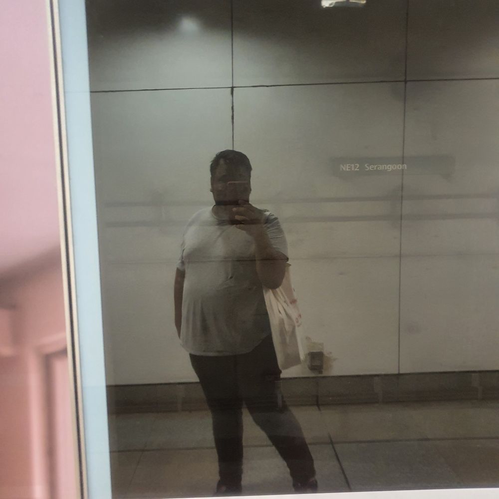 This is me, on the way home. I struck a pose while waiting for the train and took a photo of myself striking said pose lol.

 I was dressed in a large grey t-shirt and maroon pants; and I am carrying a large tote. (Shoes not visible from the image lol)

There is a sign inside the tunnel that reads "NE12 Serangoon". 

For context, "Serangoon" is the name of the station and  "NE12" is an alphanumeric code for the station on a particular line. (This station in particular has an interchange with another line so it has another alphanumeric code there.)

