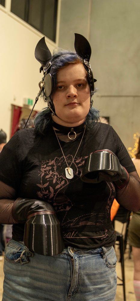 An exhausted looking trans girl with hand hooves and a day collar, in a ponygirl head harness 