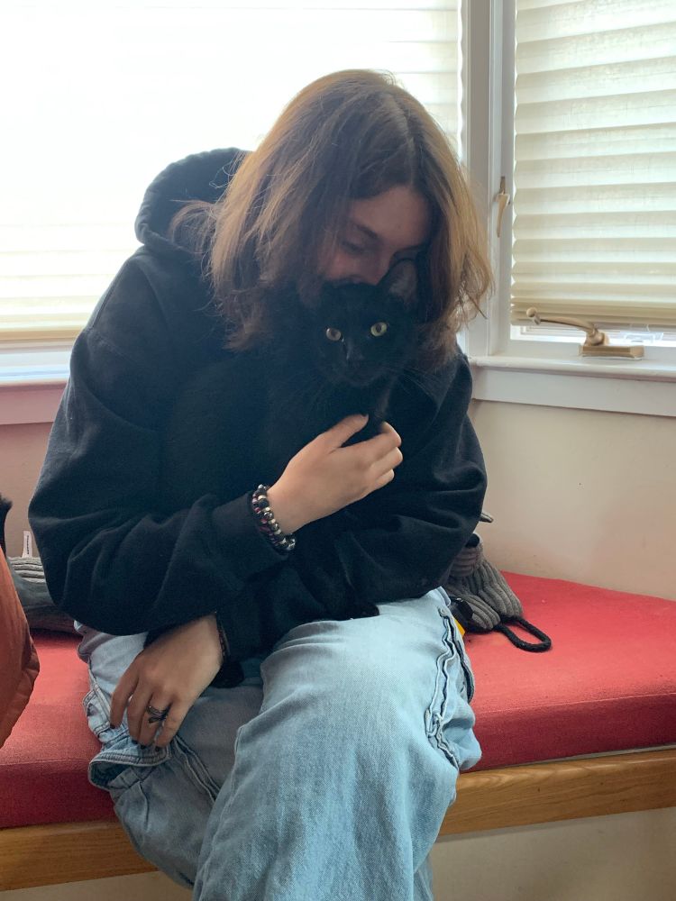 Girl holding a black cat seated on red indoor bench