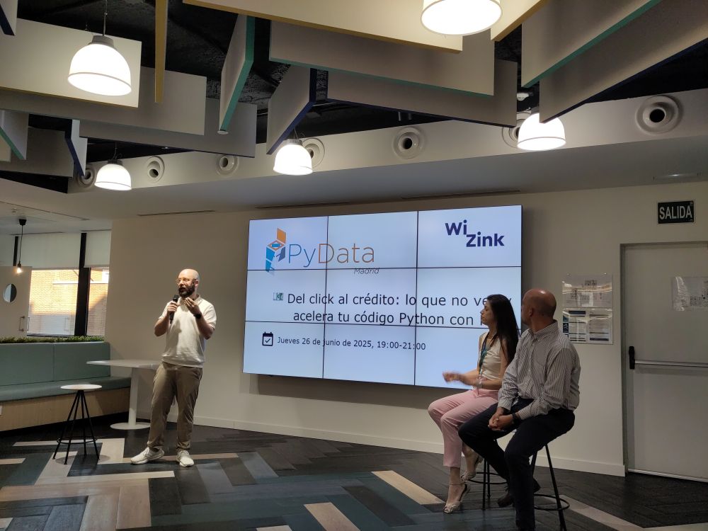 Foto de unas personas en un escenario junto a una pantalla gigante en la que se ven los logos de PyData Madrid