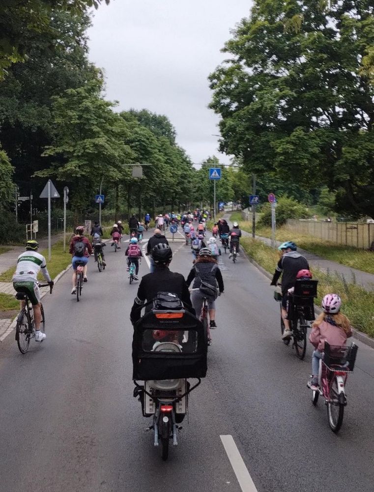 Eine große Gruppe Kinder und Erwachsener fährt in einem Fahrradkorso auf der Straße in Richtung Schule.