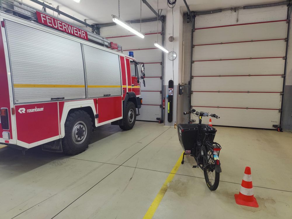 Ein Feuerwehr-LKW in der Halle, rechts daneben in ca. 2m Abstand Pylonen und ein Lastenrad im vermeintlichen Toten Winkel.