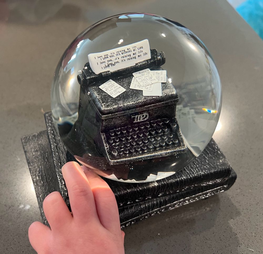 Taylor Swift Tortured Poets Department snow globe with a toddler hand reaching up from the bottom of the picture