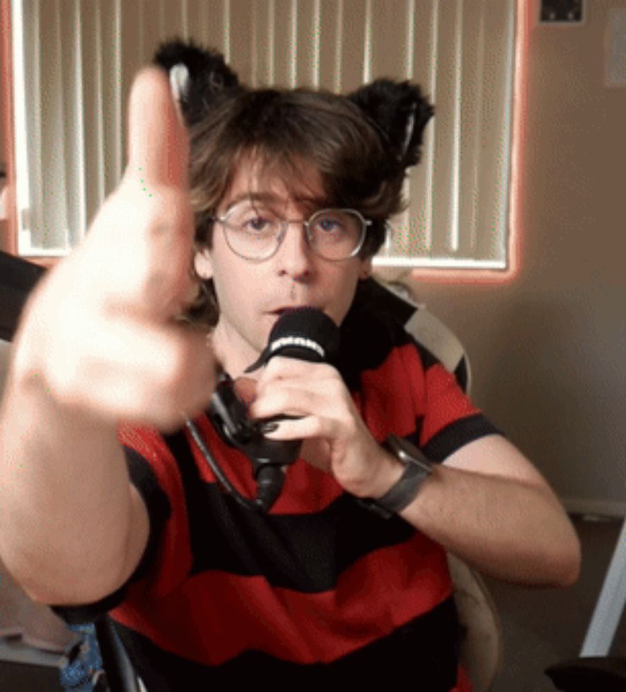 a man wearing a red and black striped shirt is holding a microphone and giving a thumbs up sign