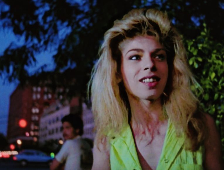 Venus Xtravaganza, a young Latina trans woman, looks off-camera and smiles. She has teased blond hair and is wearing a sleeveless fluorescent yellow blouse. She is in park in NYC at dusk, explaining reading to documentarian Jennie Livingston. Livingston went on to receive numerous awards for the resulting documentary, Paris is Burning. Venus Xtravaganza was found murdered in a hotel room in December 1988. She was 23 years old.