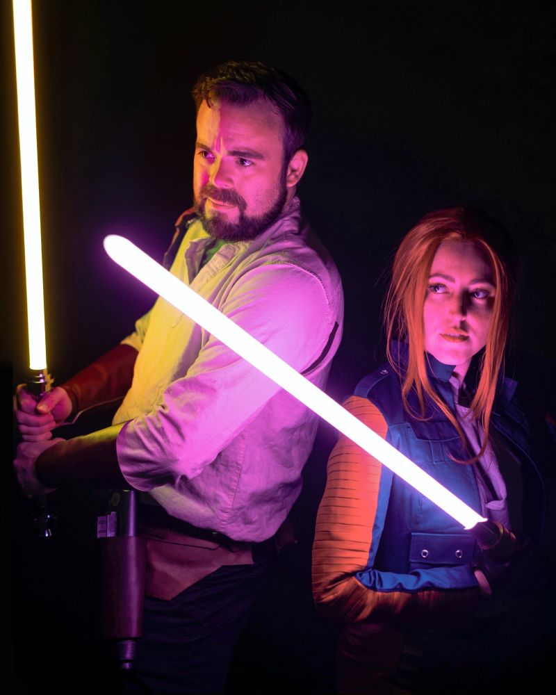 A Kyle Katarn cosplayer and a Mysteries of the Sith Mara Jade cosplayer with lightsabers raised.