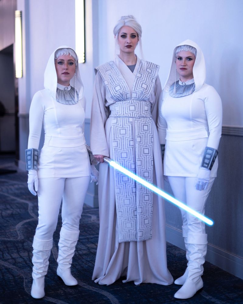 An Atris cosplayer stands between two echani handmaiden cosplayers. 