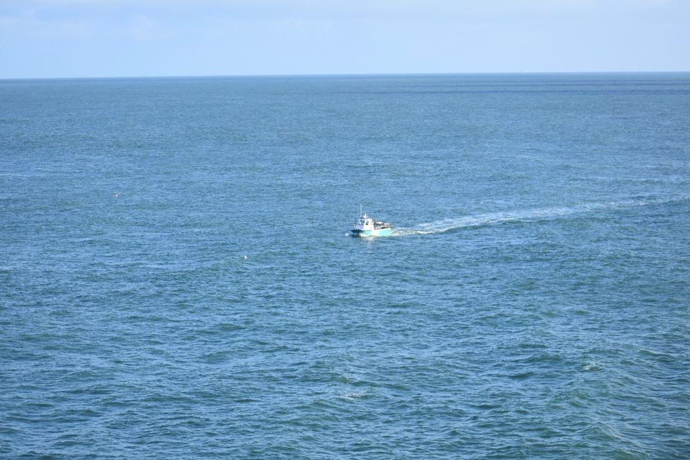 Photograph shows small fishing boat ploughing through the coastal waters off the Anglesey coast leaving its wake in the blue sea under pale blue sky