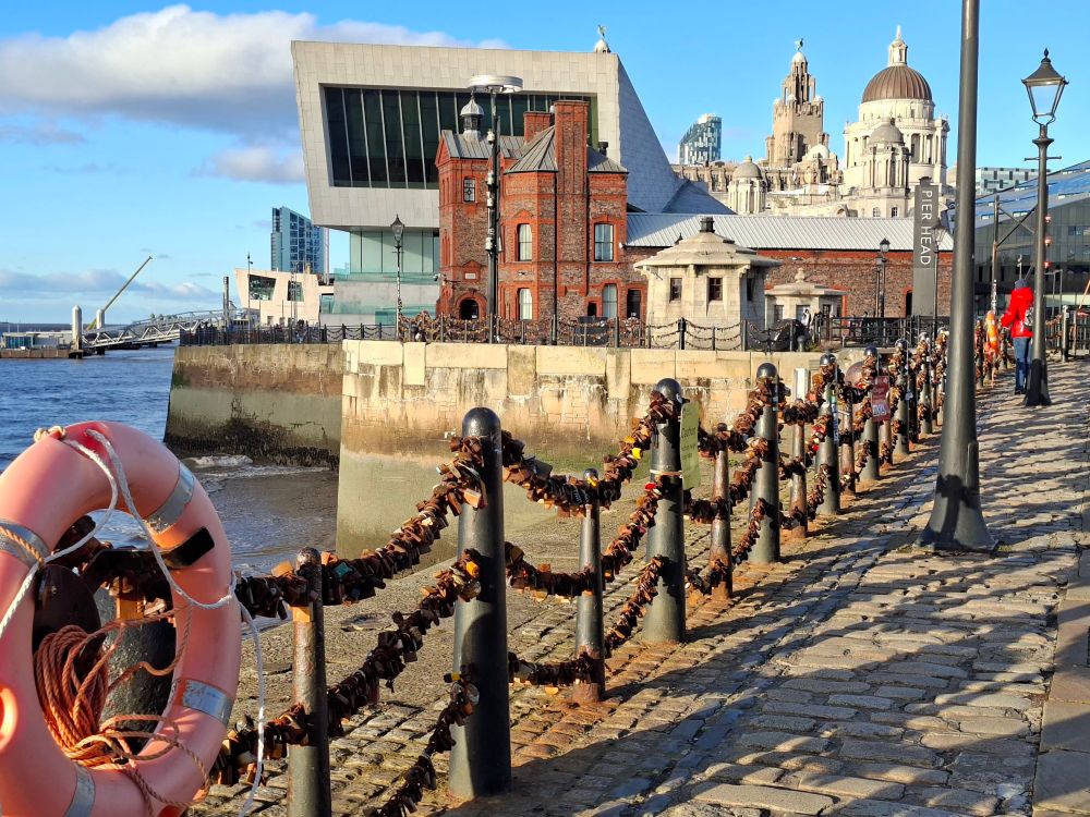 Liverpool's iconic waterfront with padlock strewn barriers in the foreground, river Mersey to the left 