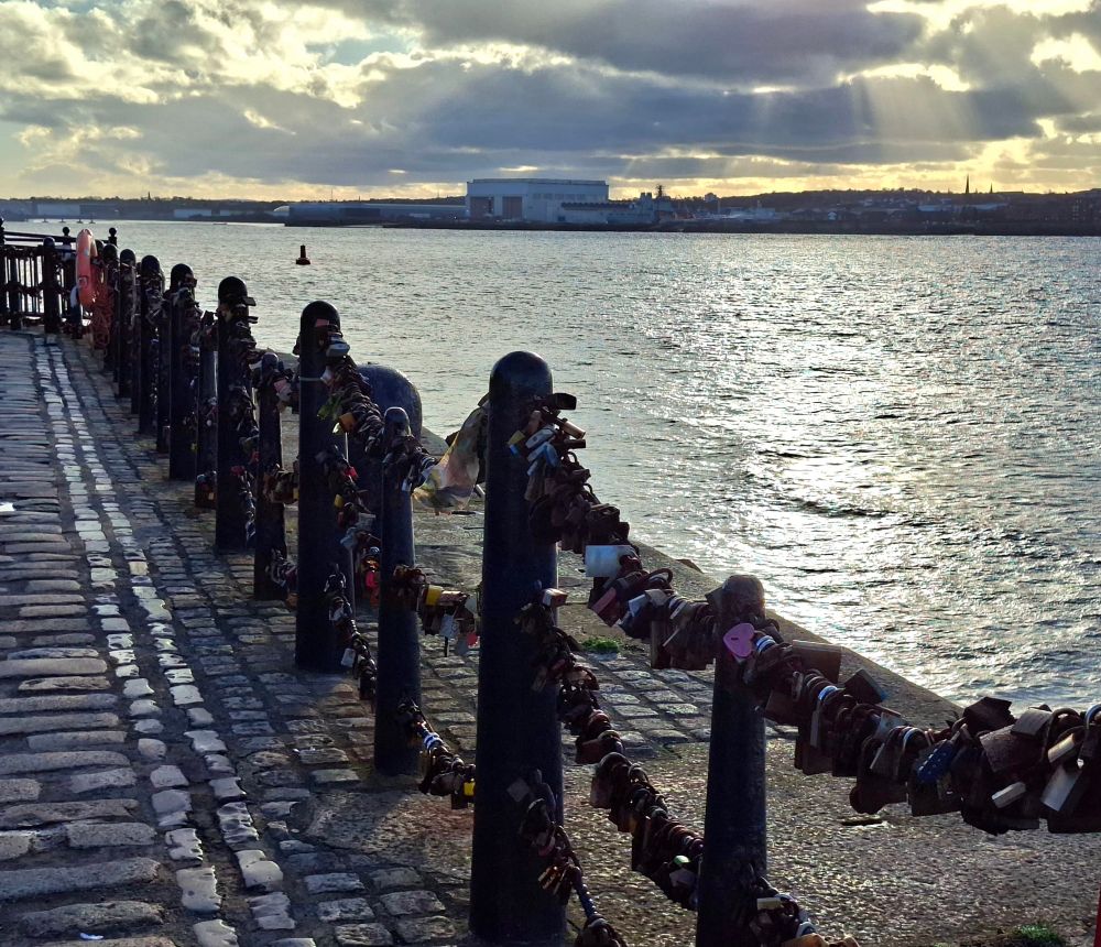 Waterfront barriers weighed down with innumerable padlocks along the River Mersey in Liverpool. Birkenhead in the distance on the far side of the river