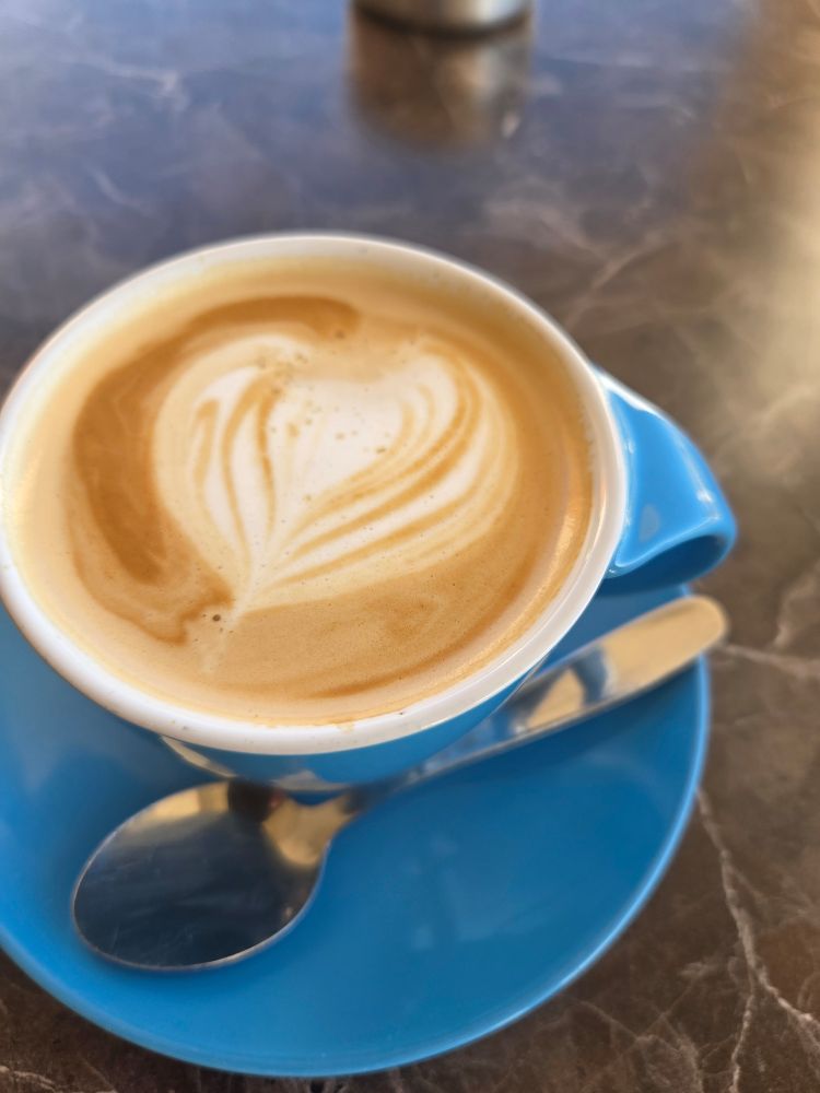 Eine Cappuccino in einer blauen Tasse. Der Schaum zeigt ein weißes Herz.