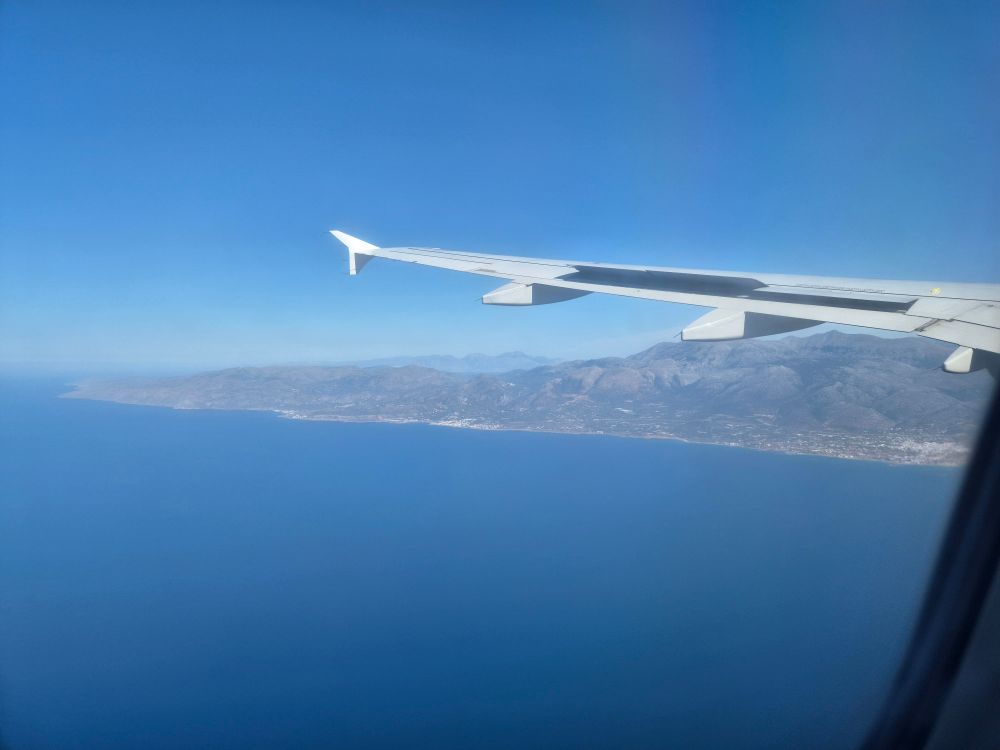 Blick aus dem Flugzeug: Landeanflug auf Rhodos. Die linke Tragfläche von hinten gesehen. Strahlend blauer Himmel, darunter blaues Meer und die Küstenlinie. 