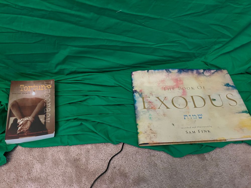 Green screen weighed down with two large books: "Torture and Democracy" and "The Book of Exodus"