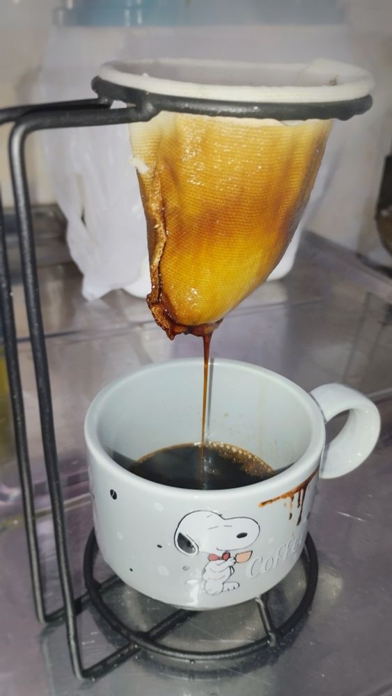 Café sendo passado pelo coador tamanho egoísta direto na xícara do Snoopy.