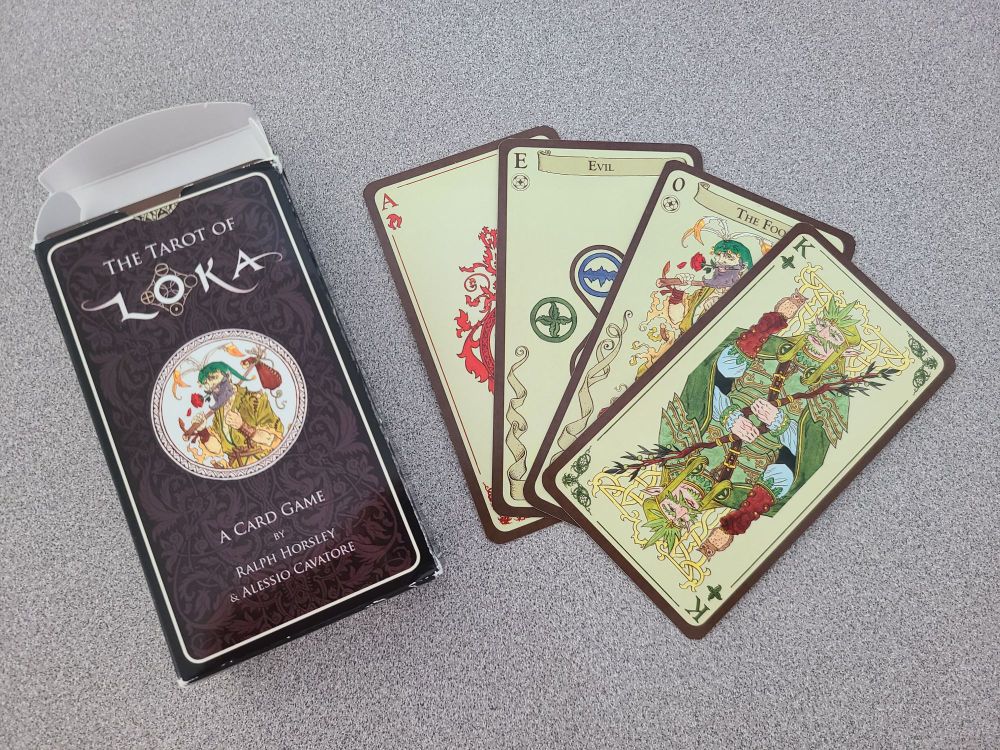The box for The Tarot of Loka next to a few of its cards (Ace of Fire, Evil, The Fool, King of Earth).