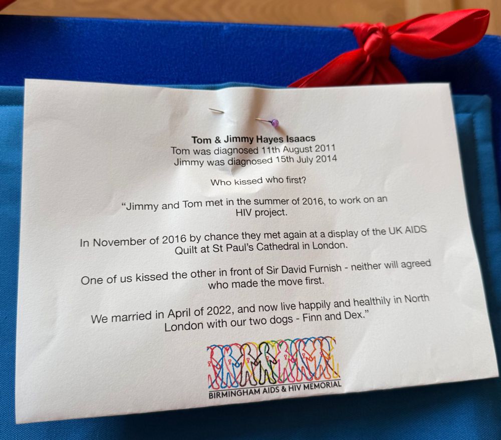 A white piece of paper with the text "Jimmy and Tom met in the summer of 2016, to work on an HIV project. In November of 2016 by chance they met again at a display of the UK AIDS Quilt at St Paul's Cathedral in London. One of us kissed the other in front of Sir David Furnish - neither will agreed who made the move first. We married in April of 2022, and now live happily and healthily in North London with our two dogs - Finn and Dex”