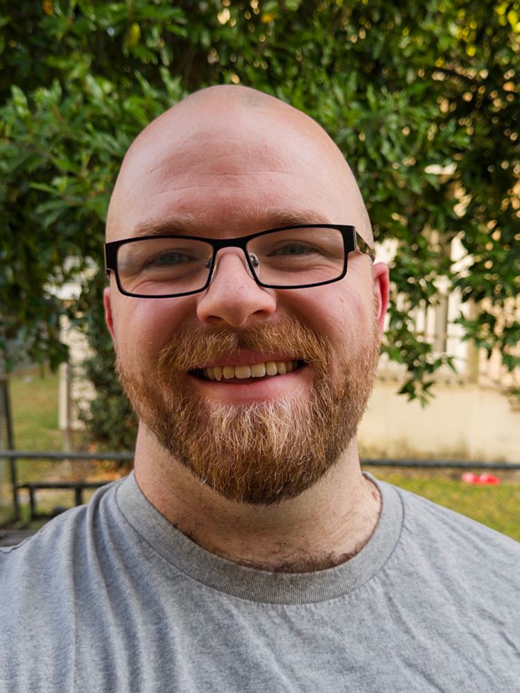 Selfie. I’m smiling at the camera. I’m in my slutty secretary black glasses and wearing a gray shirt. Bald as well!