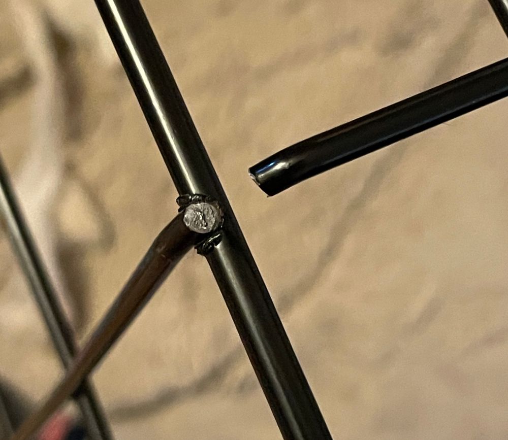 A photo closeup of a section of a broken dog crate made of black-painted 20-gauge steel wire. The wire itself has been broken, snapped in such a way where you can see the silver core. This is 1 of 6 places where the wire was snapped.